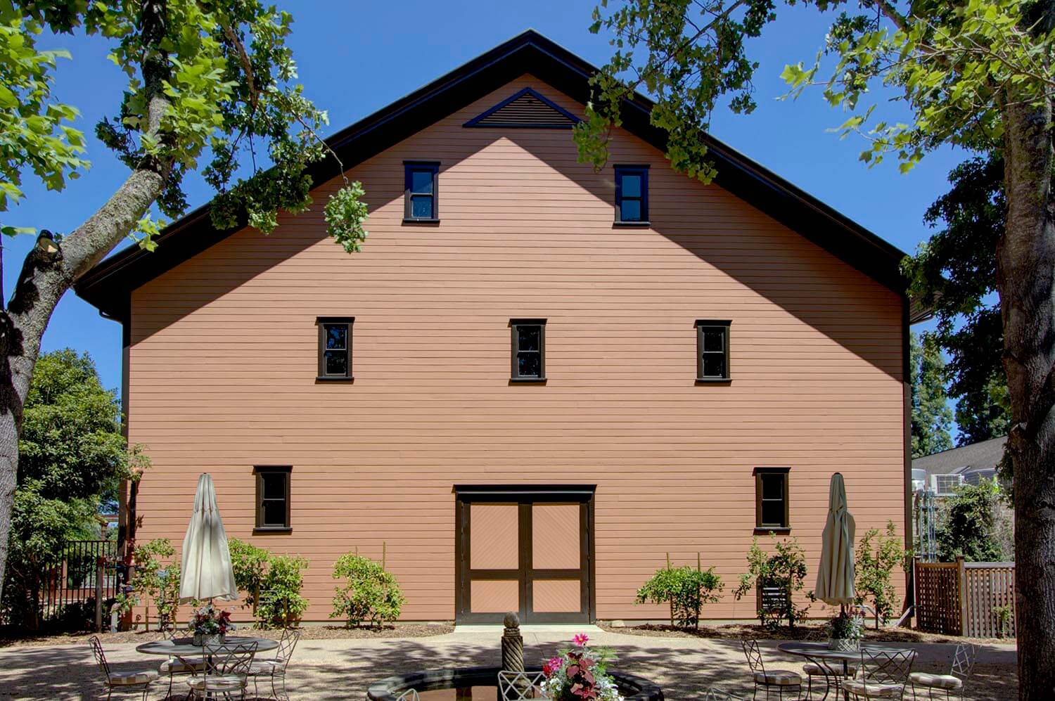 Exterior view of winery building with trees and flowers above courtyard in foreground